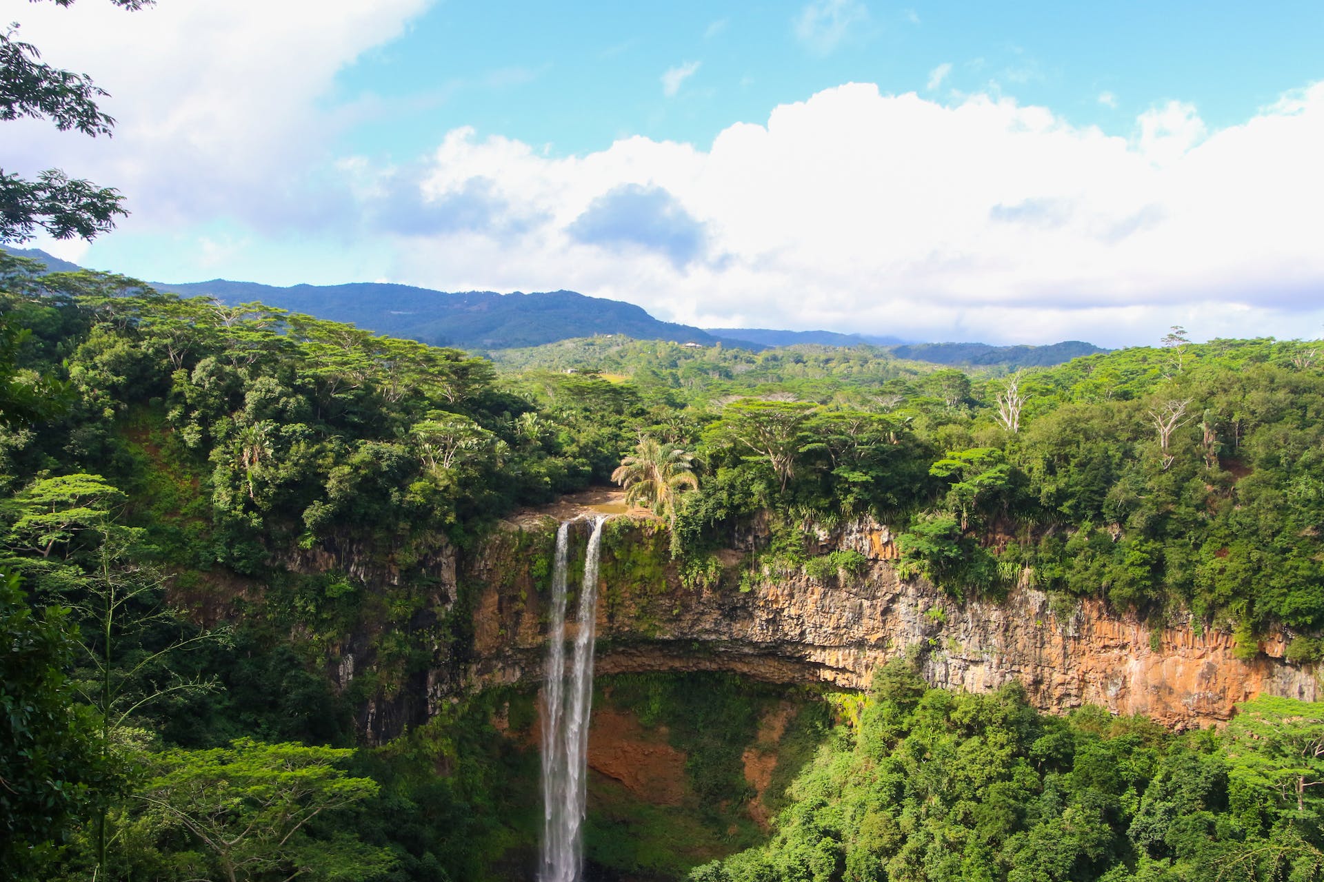 Een groen en uitgestrekt landschap met hoge tropische bomen en een smalle waterval die valt over een bauxietberg.