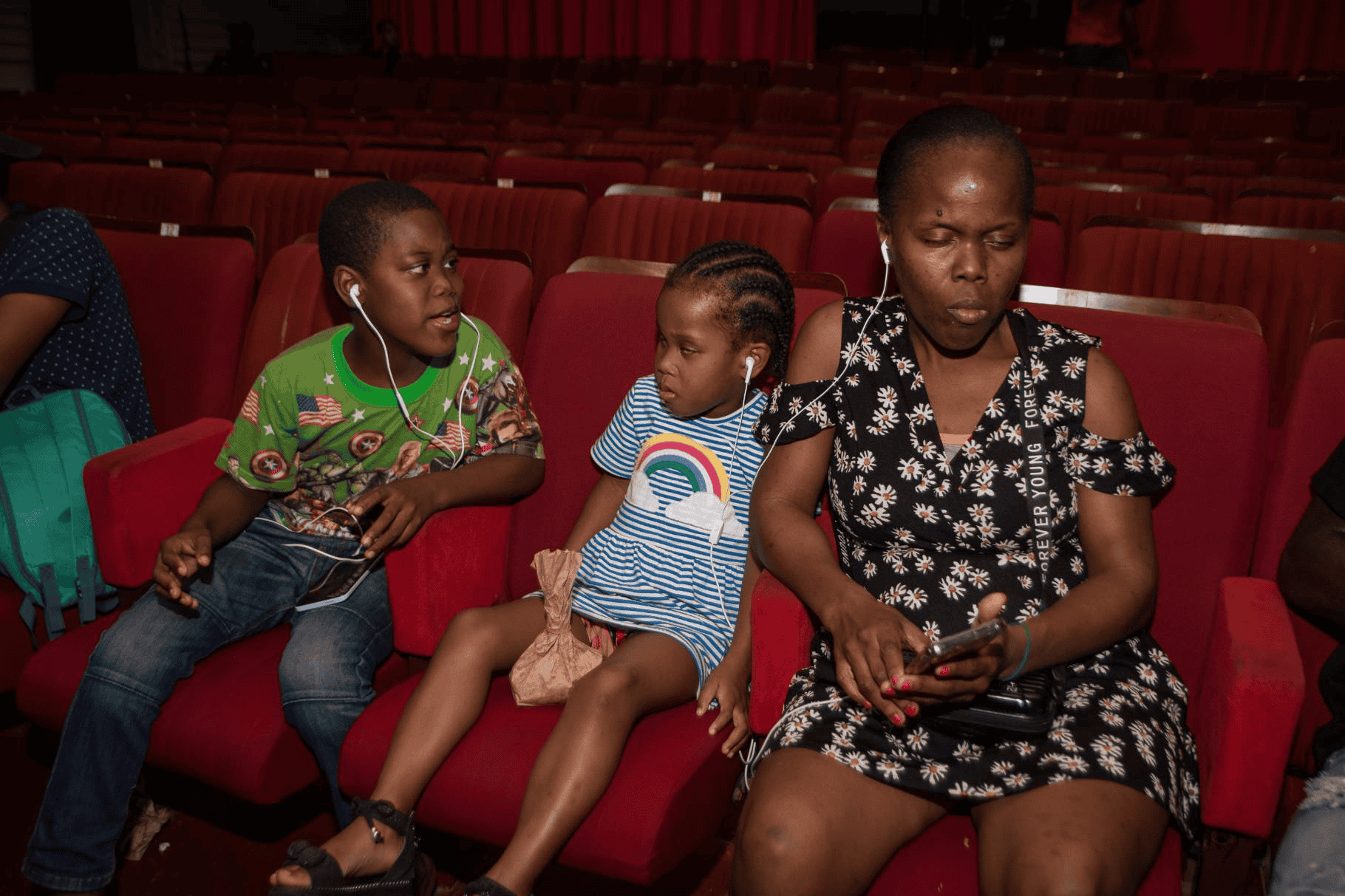 Een vrouw en twee kleine kinderen luisteren naar audiodescriptie van een film in een theater.